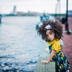 Toddler wearing girls pinafore dress in Canning fabric over mustard collared shirt leaning over Baltimore Harbor barrier.  Unique toddler clothes for you tiny style icon.